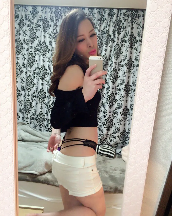 Femme latine aux cheveux châtains portant un haut blanc et un short blanc, prenant un selfie dans un miroir