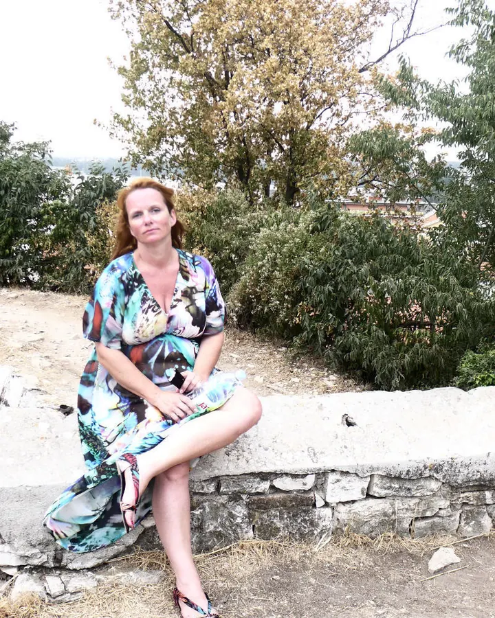 Femme blonde assise sur un muret en extérieur