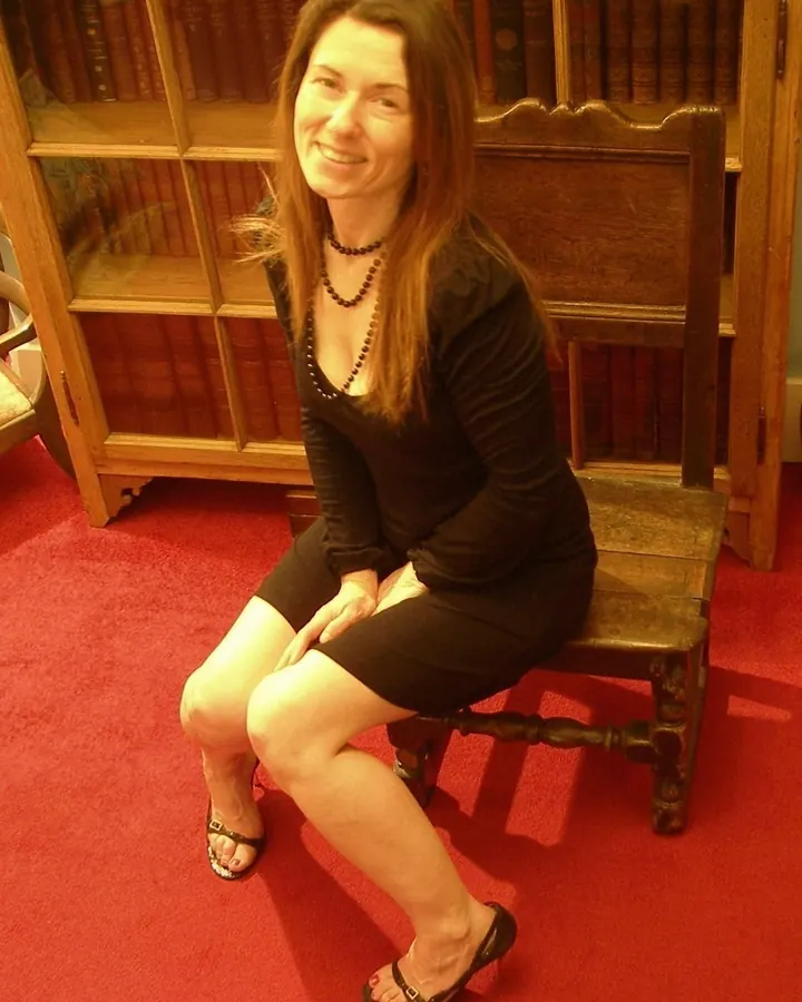 Femme brune assise sur une chaise en bois devant une bibliothèque