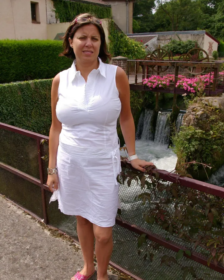 Femme aux cheveux châtains, en robe rouge et chaussures à talons, marchant sur un trottoir.