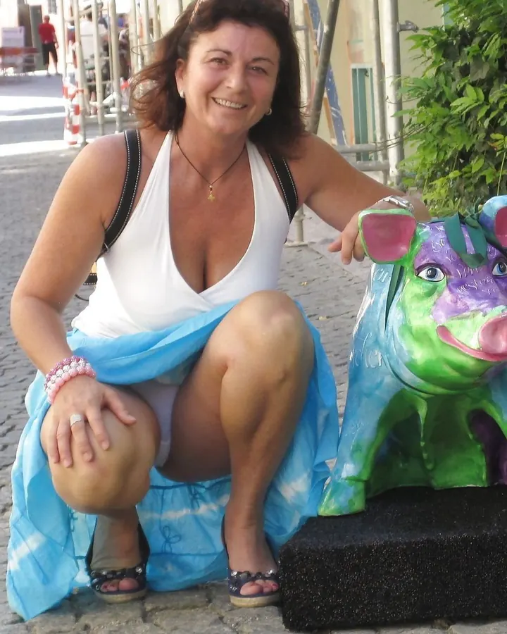 Femme aux cheveux châtains, regardant l'appareil photo, portant un haut noir et une jupe scintillante, assise dans une voiture.