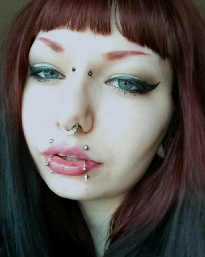 Femme aux cheveux roux portant un haut noir, souriant avec assurance devant un mur