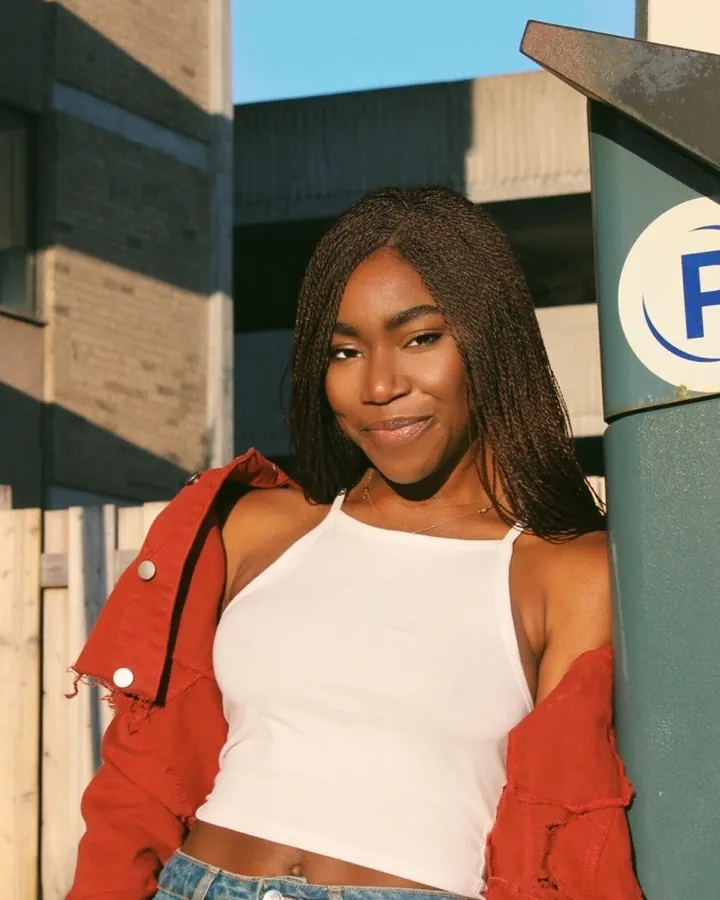 Femme aux cheveux noirs portant un haut noir, posant dans un intérieur avec un mur blanc
