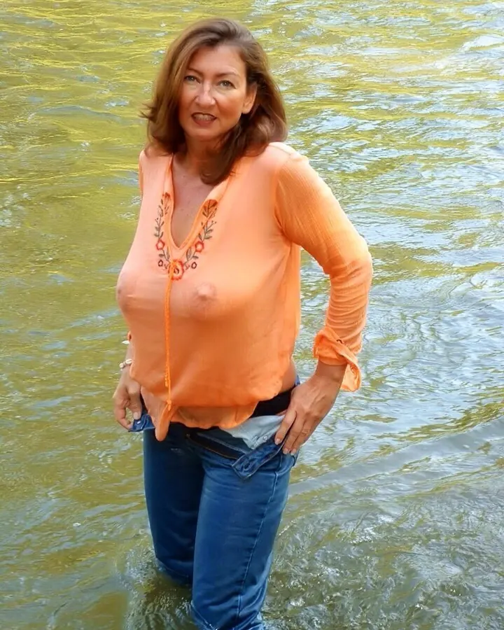 Femme en tenue orange, debout dans l'eau, tenant son haut ouvert, avec un sourire léger.