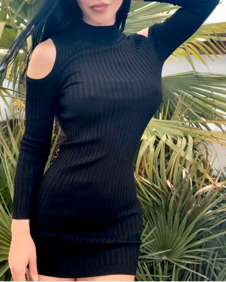 Femme aux cheveux bruns-noirs portant une robe noire ajustée avec découpes aux épaules, devant des plantes vertes.