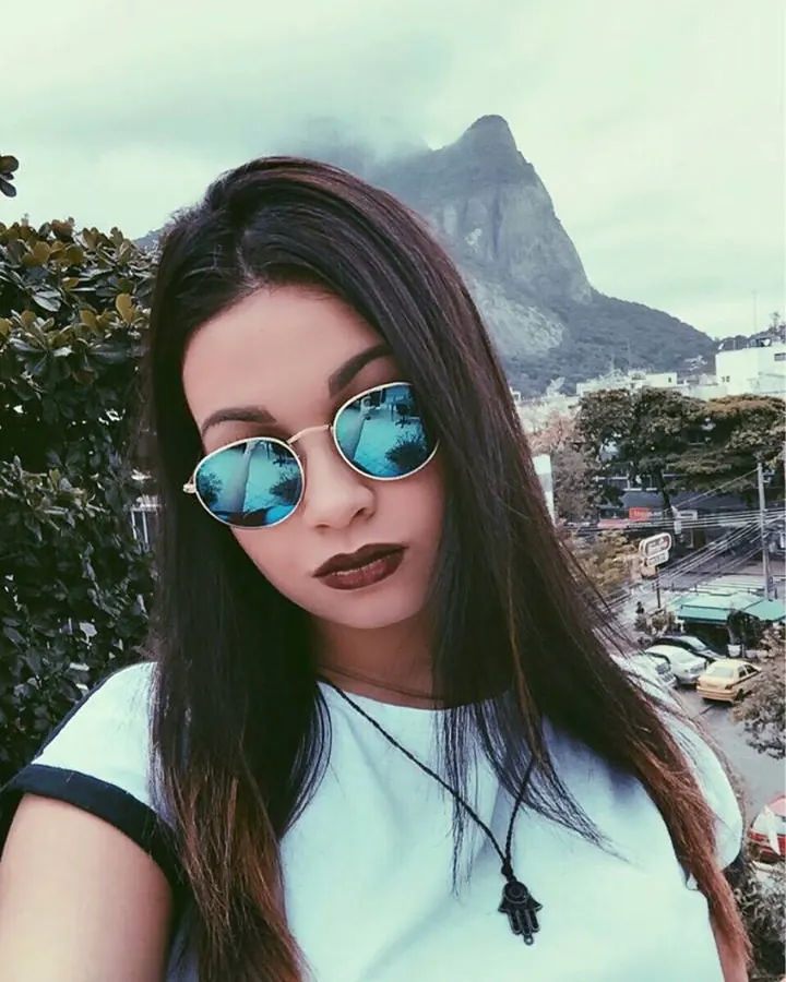 Femme aux cheveux bruns longs, portant un ensemble de lingerie noire, posant de face avec un regard direct vers l'appareil photo.