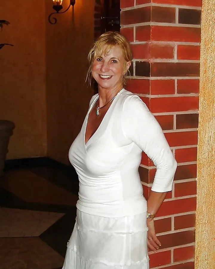 Femme blonde en lingerie noire, assise sur un canapé blanc, souriante
