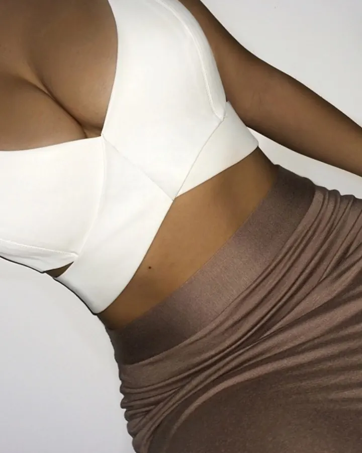 Femme africaine aux cheveux bruns, en haut blanc, assise sur un WC, souriant à l'appareil.