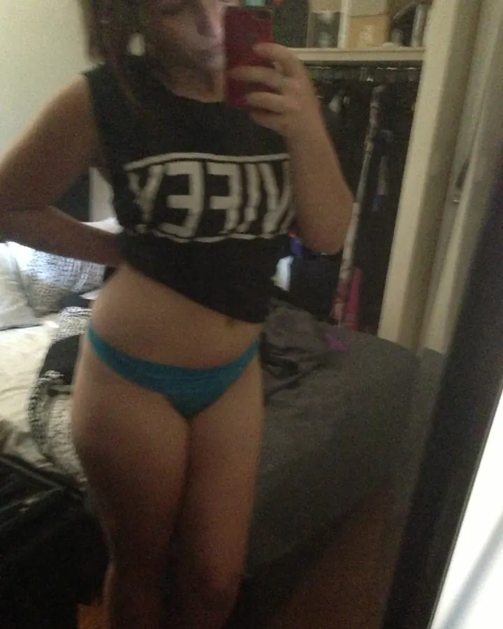 Jeune femme en tenue noire, tenant un téléphone rouge, prenant un selfie devant un miroir dans une chambre.