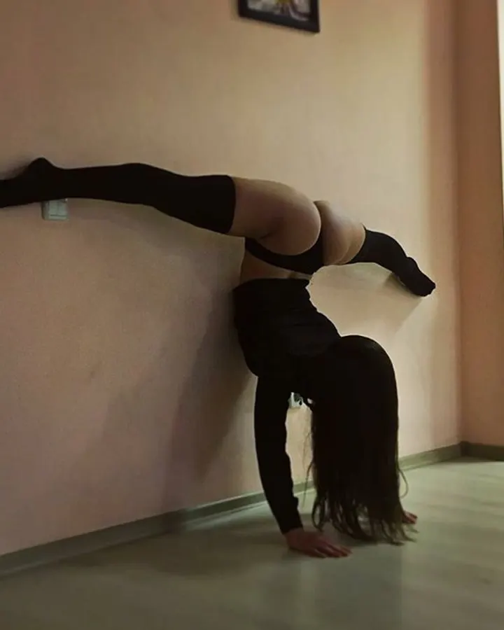 Femme en tenue noire, faisant une planche contre un mur, jambes tendues, cheveux longs tombant vers le sol.