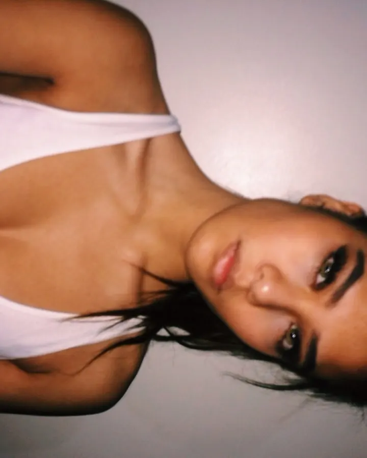 Jeune femme en body blanc, allongée sur le côté, tête inclinée, regardant l'appareil, cheveux noirs.