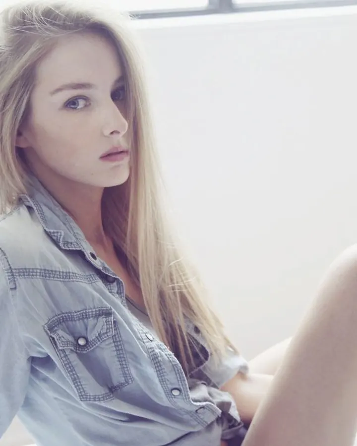 Jeune femme blonde en chemise décontractée, assise sur un lit blanc, regardant l'objectif