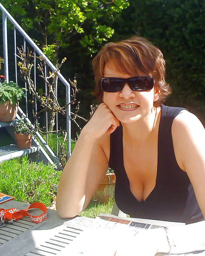 Femme en haut noir profond, lunettes de soleil, souriante en terrasse verdoyante