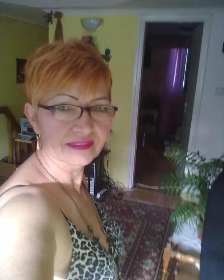 Femme aux cheveux roux courts portant des lunettes, un haut léopard, souriant à l'appareil dans un salon