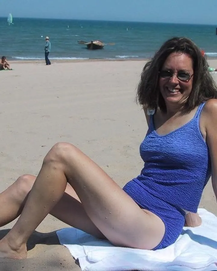 Femme en maillot de bain bleu, souriante, assise sur une serviette blanche sur une plage