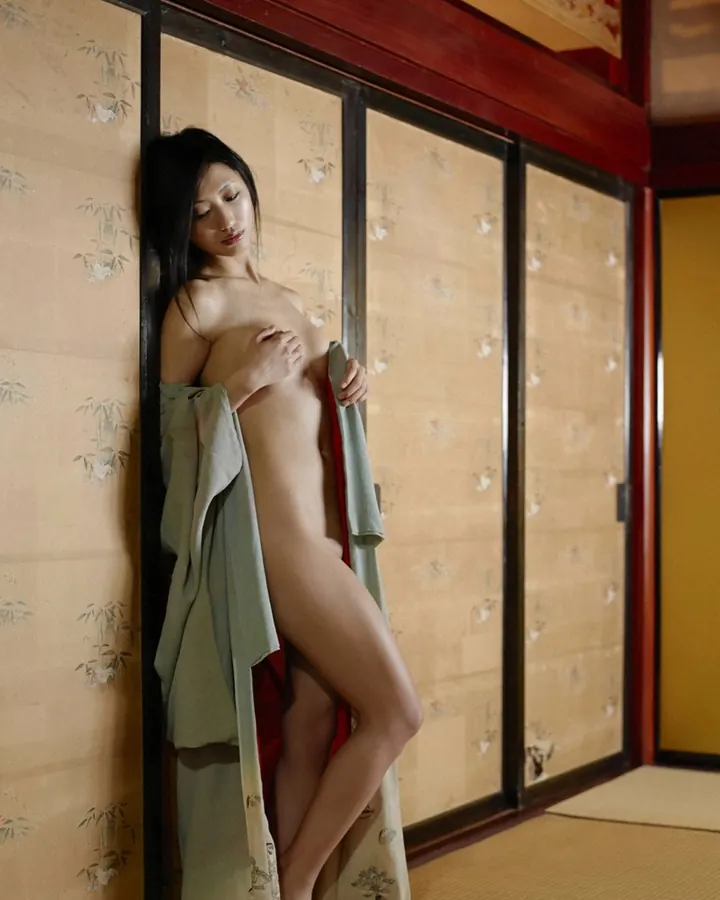 Femme asiatique aux cheveux noirs, nue sous un kimono vert, adossée à un shoji dans une pièce japonaise.