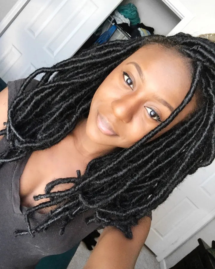 Femme aux cheveux noirs portant un haut noir et un short jaune, prenant un selfie devant un miroir dans une chambre.
