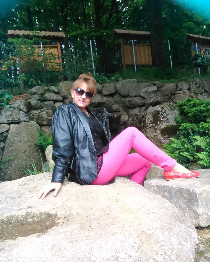 Femme blonde en lingerie blanche, debout devant une clôture en bois, portant des chaussures à talons noirs.