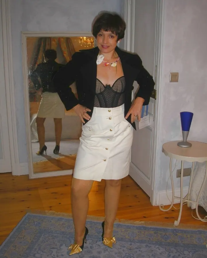 Femme aux cheveux bruns-noirs en tenue élégante, posant dans une chambre avec miroir