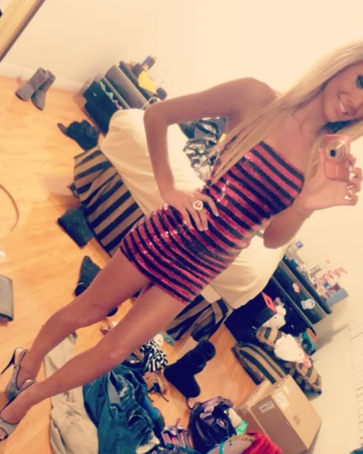 Jeune femme blonde, en tenue noire, prenant un selfie dans un miroir, regard vers l'appareil.
