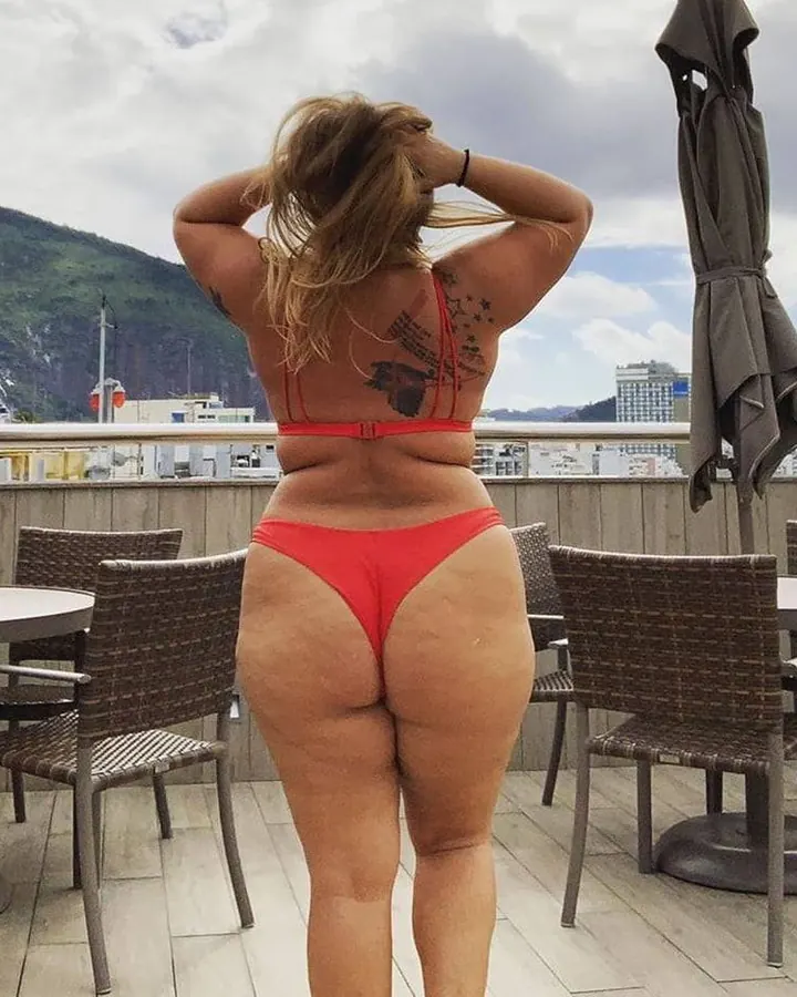 Femme aux cheveux blonds, vue de dos, en maillot rouge, sur une terrasse, montagne en arrière-plan.