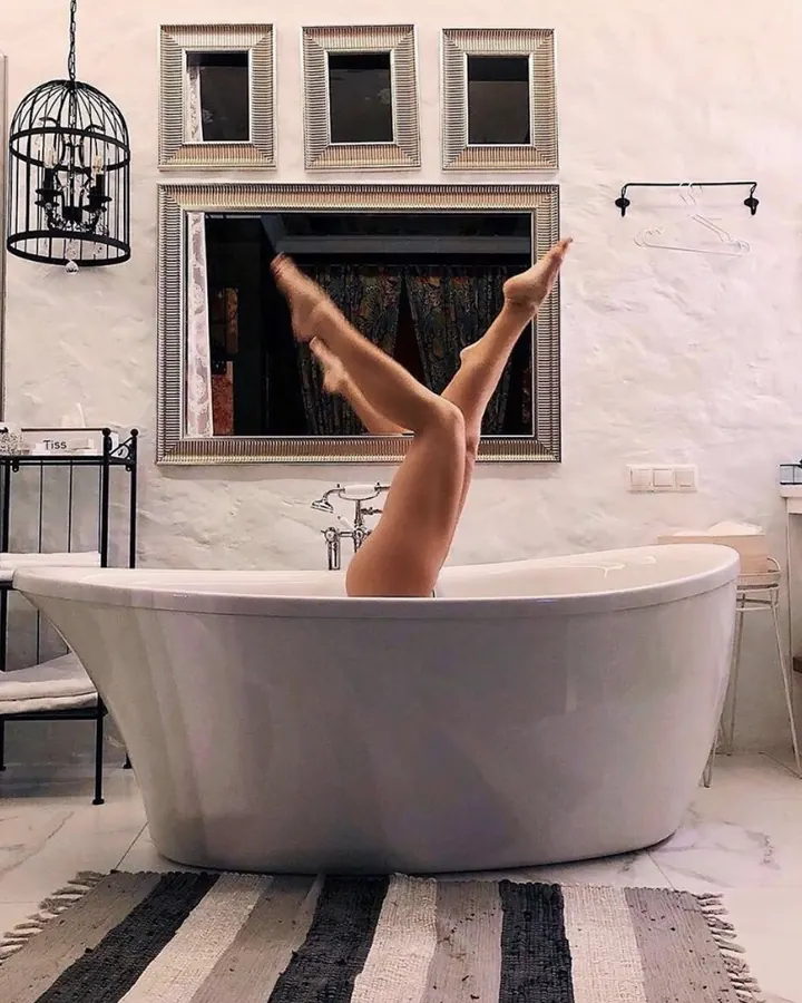 Jambes féminines sortant d'une baignoire blanche dans une salle de bain élégante, les pieds levés vers le plafond