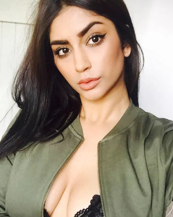 Femme aux cheveux bruns foncés, portant un haut vert olive, regardant vers l'appareil, le haut ouvert sur un soutien-gorge noir en dentelle