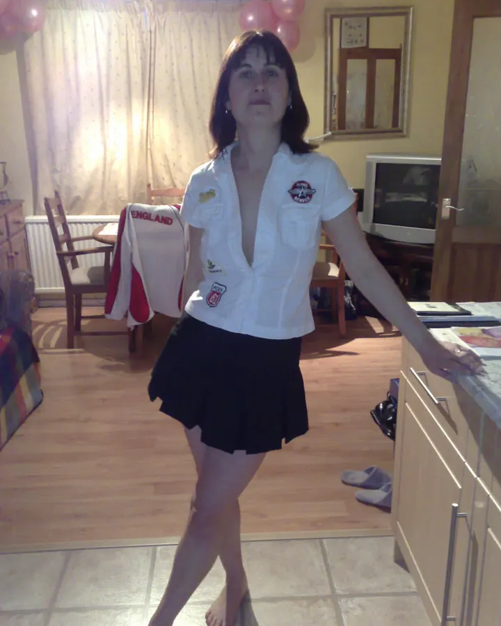 Femme aux cheveux bruns portant une chemise blanche et une jupe noire dans un salon avec ballons roses