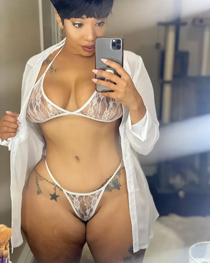 Femme aux cheveux bruns-noirs en body noir, vue de dos, prenant un selfie dans un miroir, main sur la hanche.