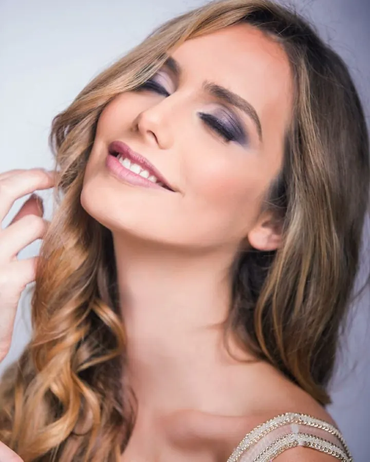Femme aux cheveux bruns, portant un haut blanc, en gros plan, dans une pièce aux murs sombres
