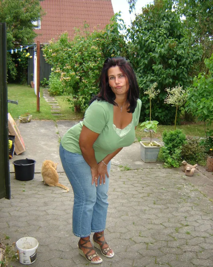 Femme aux cheveux bruns, portant un haut vert et un jean, dans un jardin avec un chat orange