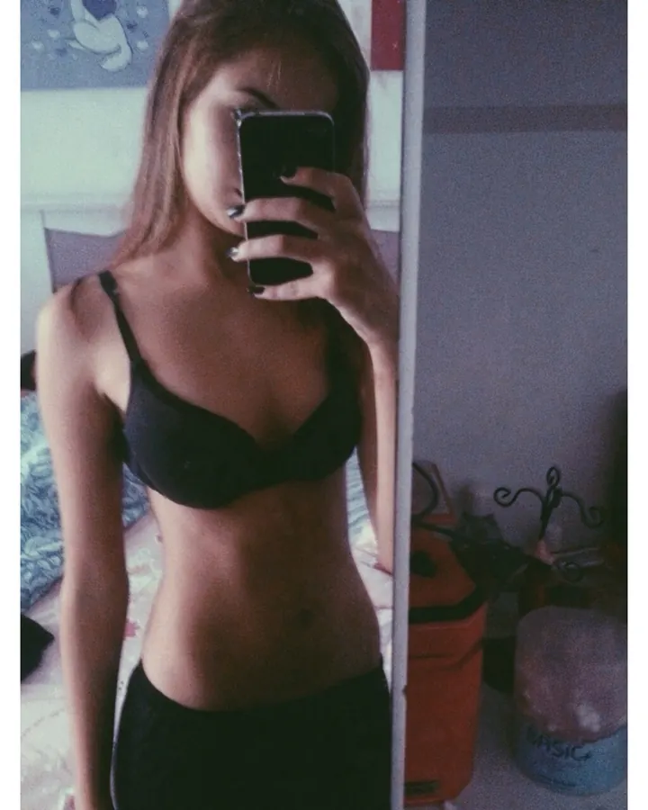 Femme blonde souriante, portant un haut noir à col cœur, debout près d’une voiture blanche, avec des collants à mailles