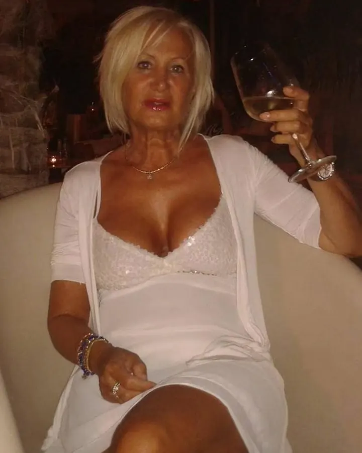 Femme blonde en chemise grise, assise à un bureau, regardant l'appareil, lunettes sur le nez.