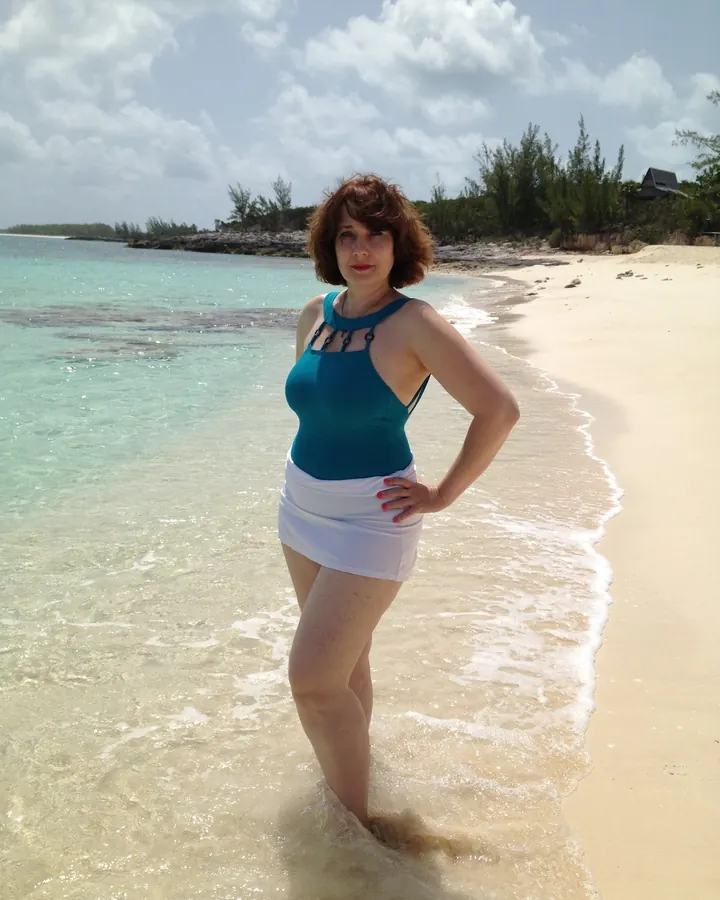 Femme en bikini noir et multicolore, sur une plage, dos tourné vers l'océan.