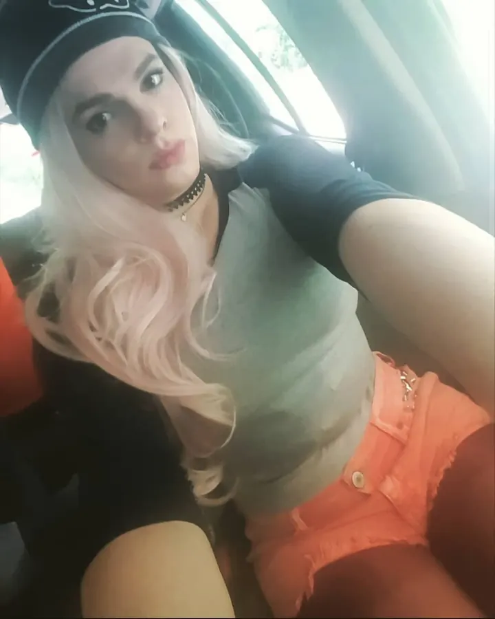 Femme trans aux cheveux blonds, en tenue noire, debout sur un escalier industriel