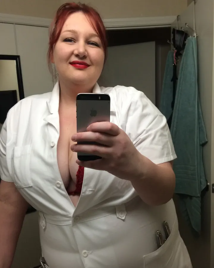 Femme aux cheveux roux en blouse blanche avec soutien-gorge rouge, prenant un selfie