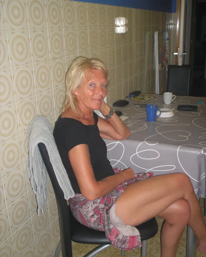 Femme blonde en haut bleu debout près d'une table, regardant l'appareil