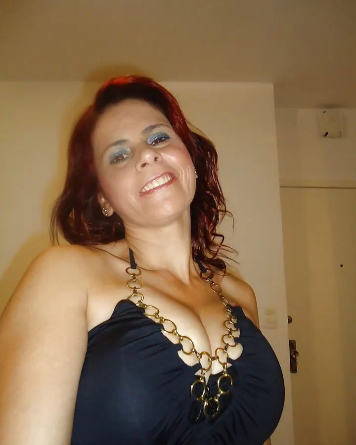 Femme aux cheveux roux en haut noir avec collier doré, souriant à l'appareil