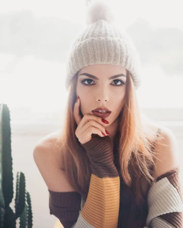 Femme en bonnet tricoté blanc, gant de laine marron, regardant l'appareil avec doigt sur la bouche