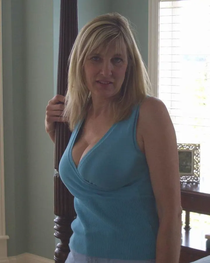 Femme blonde en haut bleu tenant une barre de bois, regardant directement l'appareil