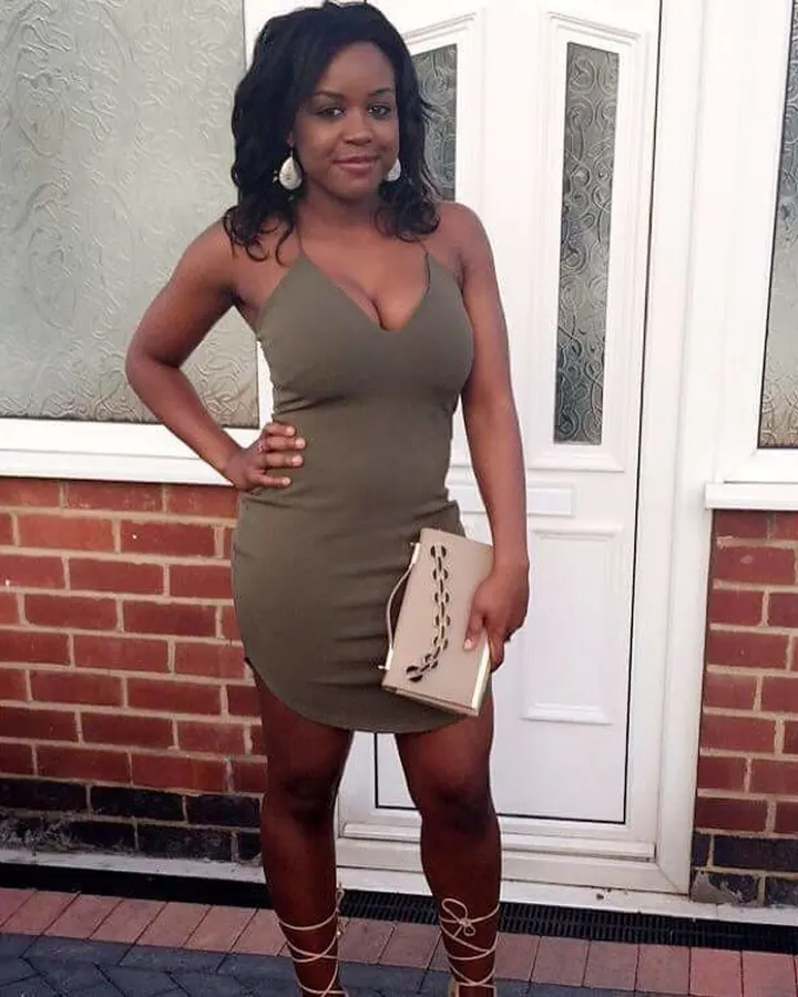 Femme africaine en robe verte ajustée, posant près d'un pot de fleurs colorées dans un jardin.